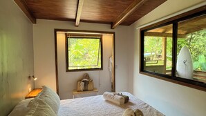 A bedroom with a wooden ceiling, a large window, a bed with patterned bedding, and a small bedside table with a lamp. - Feeling Trees Jungle Lodge-Casa Caracoles walking distance to the beach (Cabuya)