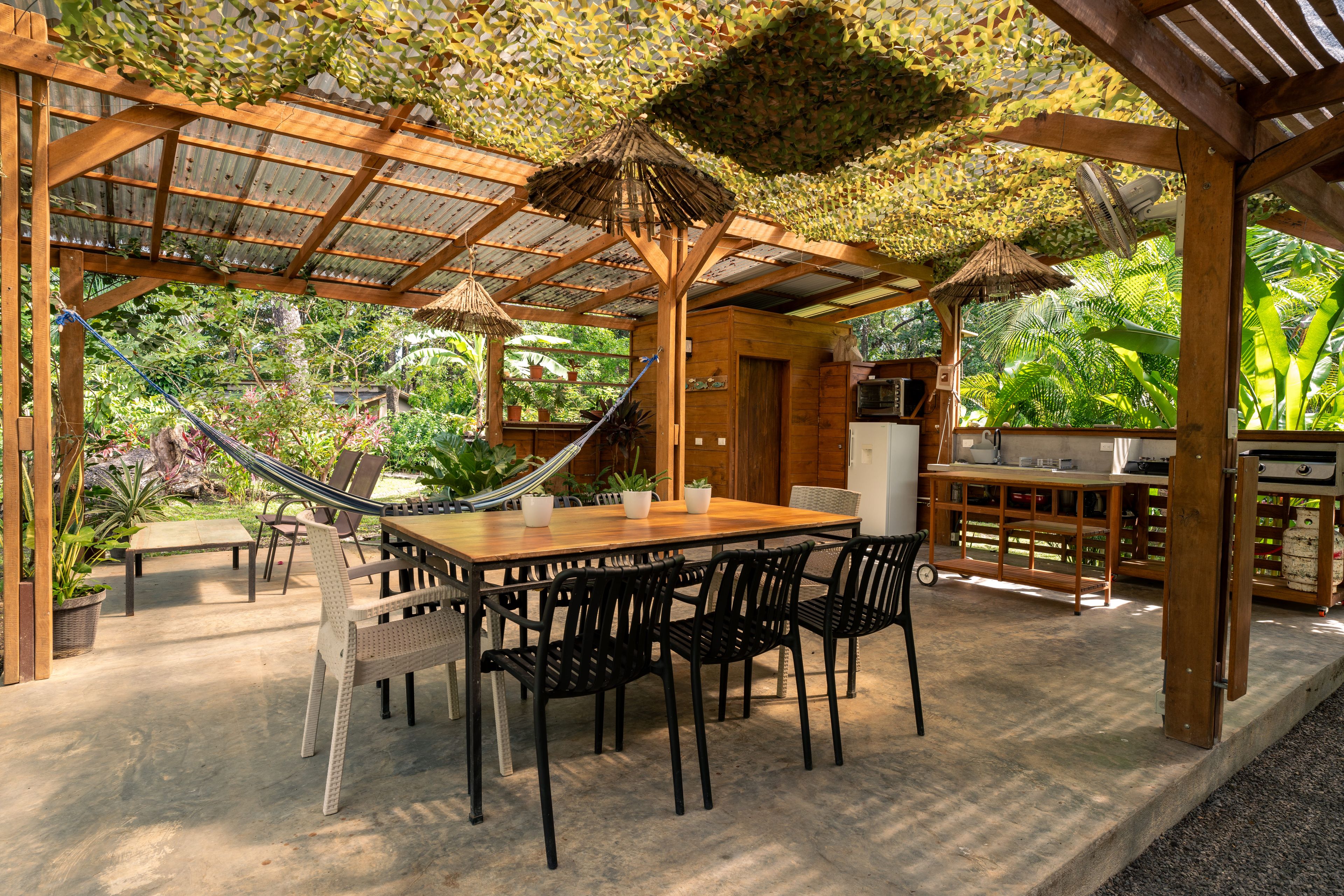 Een terras buiten met een houten tafel en stoelen, een hangmat en een barbecueplaats.