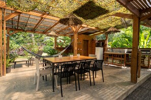 An outdoor patio with a wooden table and chairs, a hammock, and a grill area. - Caracoles · Jungle Cabin for 2 · Pool + Walk to Beach · Cabuya (Cabuya)