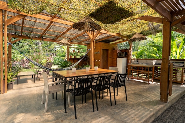 Une terrasse extérieure avec une table et des chaises en bois, un hamac et un espace barbecue.
