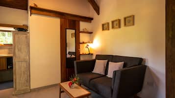 Una sala de estar acogedora con un sofá de color gris oscuro, una mesa de centro de madera con un jarrón, y una cocina visible a través de un puerta abierta.