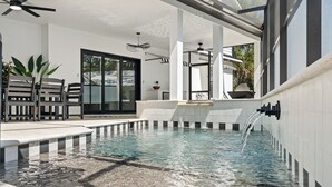 Una piscina interior moderna con agua cristalina, un ventilador de techo y una zona de estar con sillas y una mesa.