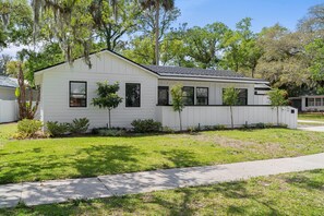 Stunning single-story home with a gabled roof and inviting front porch, set amidst a beautifully manicured lawn and lush trees.