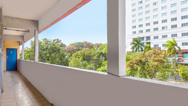 A corridor with a blue door, a white wall, and a view of a tall building and trees. - Hotel O Hasan House SyariahNearPelabuhan Feri Harbor Bay (Batam)