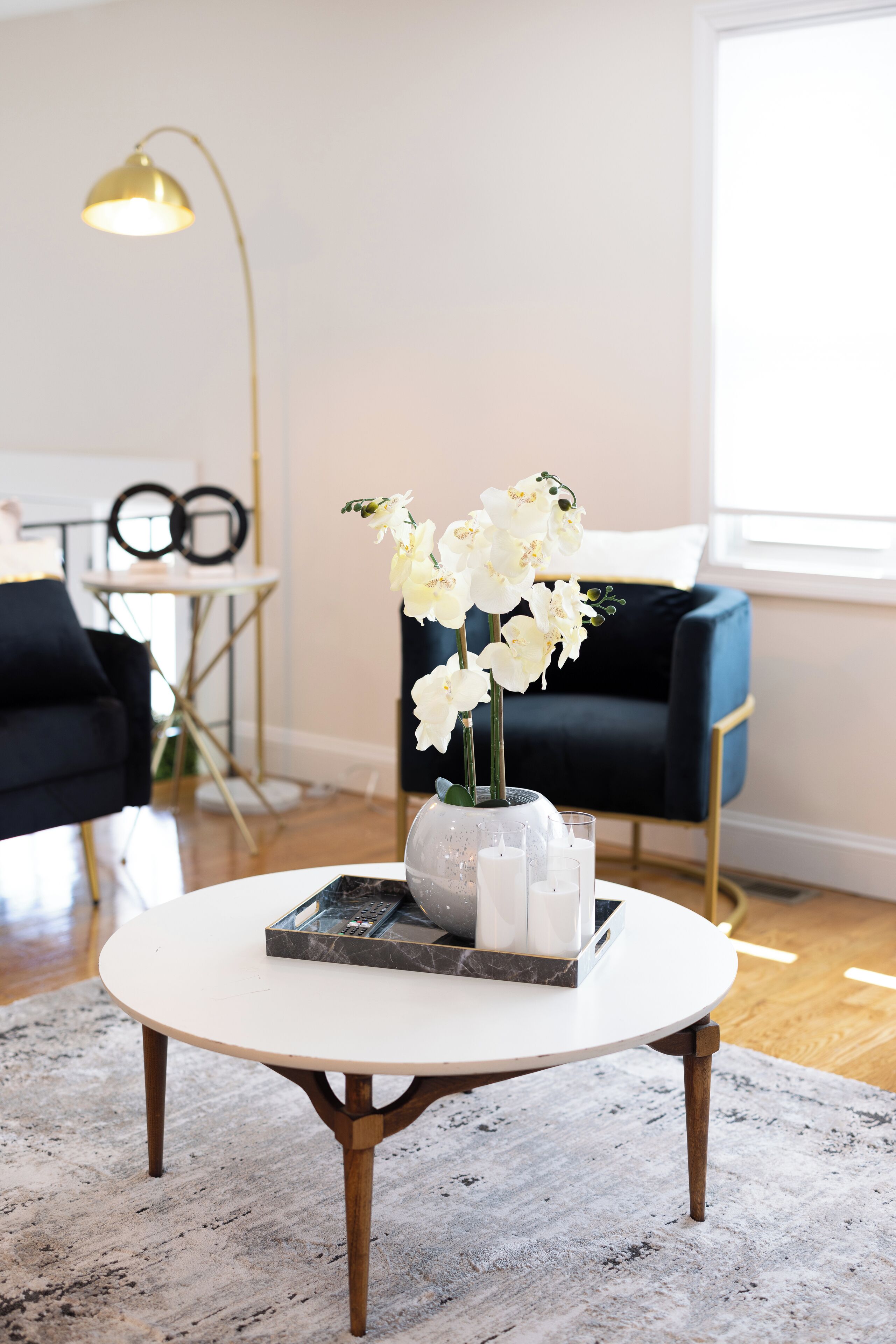 A round coffee table with a vase of white flowers, a book, and a glass of water.