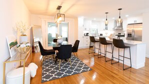 Uma cozinha moderna com armários brancos, uma ilha central com banquetas e iluminação pendente.