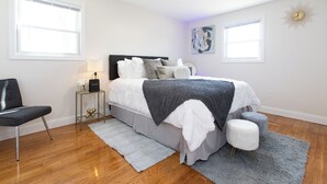 Quarto com cama, cadeira, mesa de cabeceira e relógio na parede.