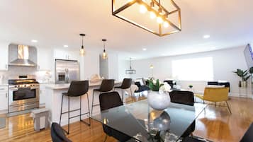 A modern kitchen with stainless steel appliances, a dining area with a glass table and black chairs, and a large window providing natural light.