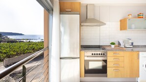 A compact kitchen with a view of the ocean, a stainless steel refrigerator, a stove, and wooden cabinets. - Beautiful duplex seafront in Playa San Juan with awesome views !!! (Guía de Isora)
