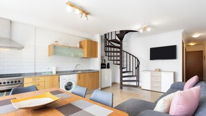 A modern kitchen with a built-in stove, a dining area with a table and chairs, a grey sofa with cushions, and a spiral staircase leading to another level. - Beautiful duplex seafront in Playa San Juan with awesome views !!! (Guía de Isora)