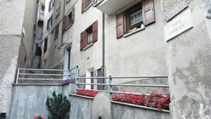 A narrow urban street with a stone wall, a small fountain, and flower boxes. - Ursula House - Your Mountain Holiday (Premana)