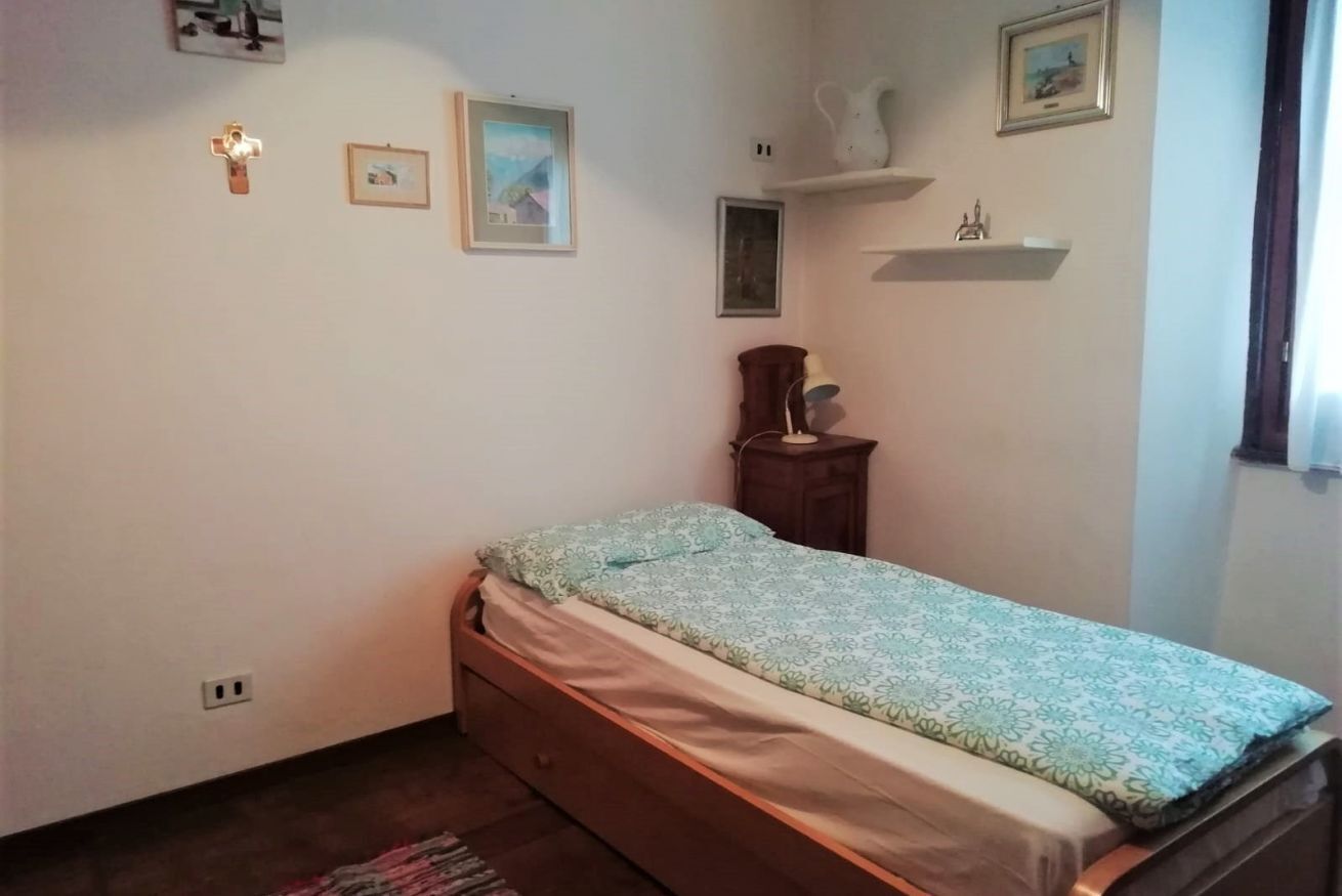 A small, neatly arranged bedroom with a single bed, a nightstand, a lamp, and a few wall-mounted shelves with decorative items.