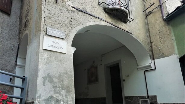 An entrance with a sign reading "Piazza Consiglio" and a stone archway. - Ursula House - Your Mountain Holiday (Premana)