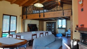 A spacious living area with a high wooden ceiling, a dining table with chairs, a sofa, and a fireplace. - Cascina Cà Scarlatta - Your Mountain Holiday (Introbio)