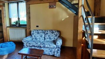Uma sala de estar acolhedora com um sofá estampado, uma mesa de centro de madeira, um puff azul, um radiador e uma escada.