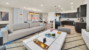 A modern living room with a sofa, coffee table, and a kitchen area with dark cabinets and a white countertop. - Family Fun Game Room with Pool and Spa-3616LL (Davenport)