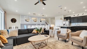 A modern living room with a black sofa, beige armchairs, a round coffee table, and a dining area with a kitchen in the background. - Spacious 10Bed Pool Home with Game Room-4265LA (Davenport)