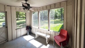 Uma sala de sol com grandes janelas, um ventilador de teto, um banco e uma cadeira vermelha.