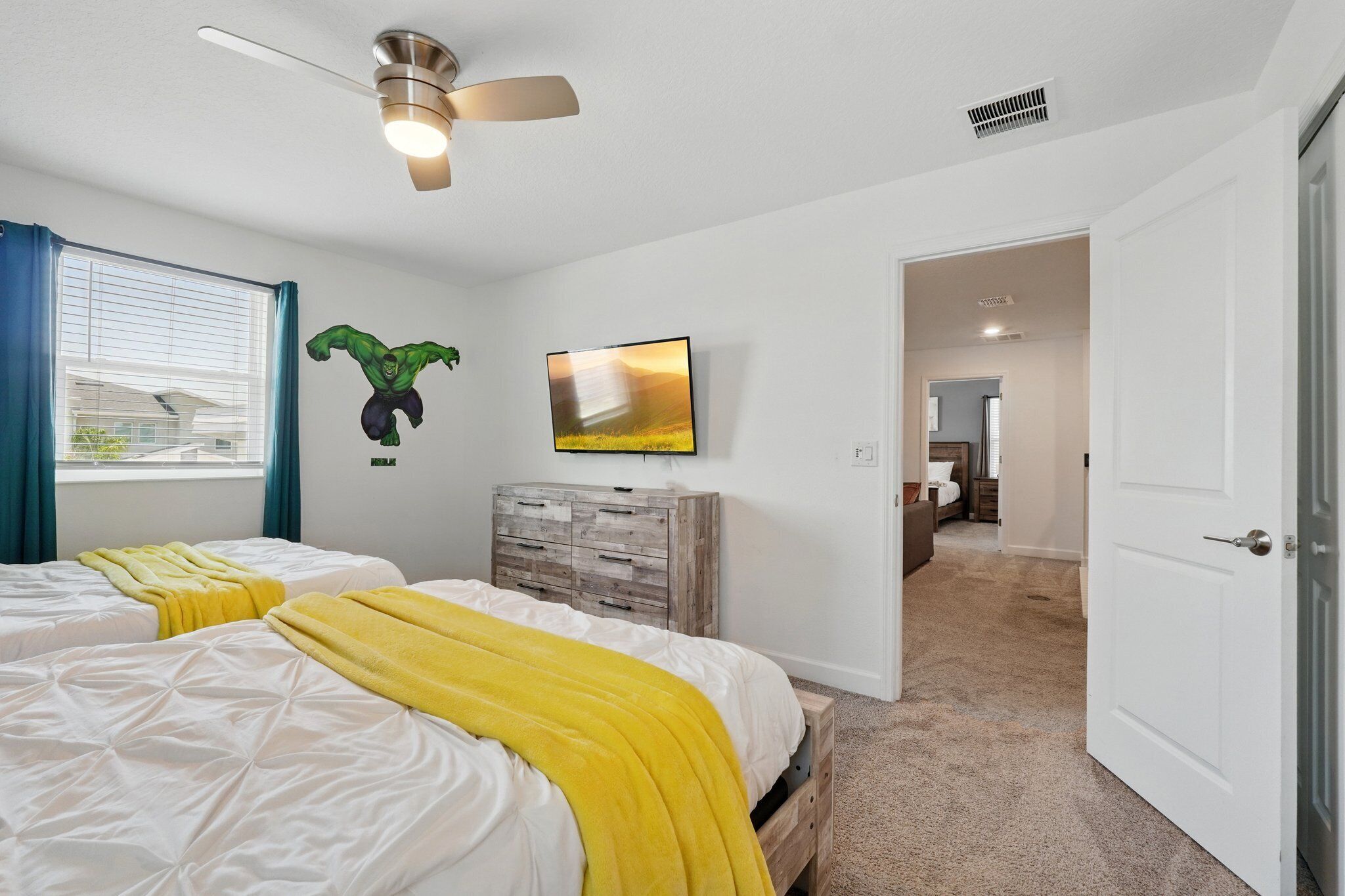 A bedroom with two beds, a ceiling fan, a TV, and a wardrobe.