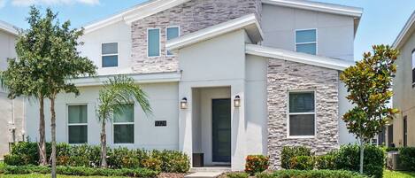A modern two-story house with a stone facade, a front door, and a small porch.