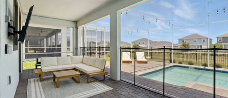 A modern outdoor living area with a sectional sofa, a wooden coffee table, and a pool view.