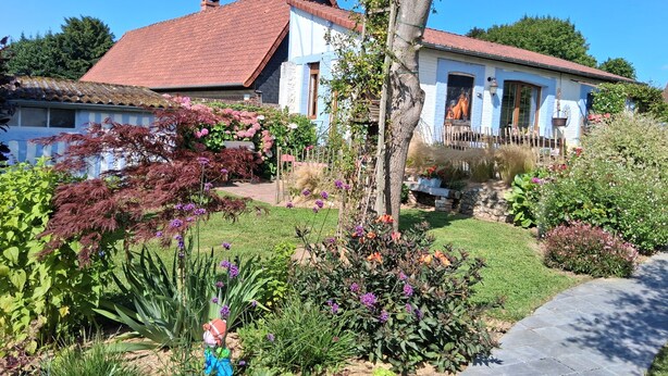 Una casa con techo de tejas rojas, fachada blanca y un jardín bien cuidado con diversas plantas y flores.