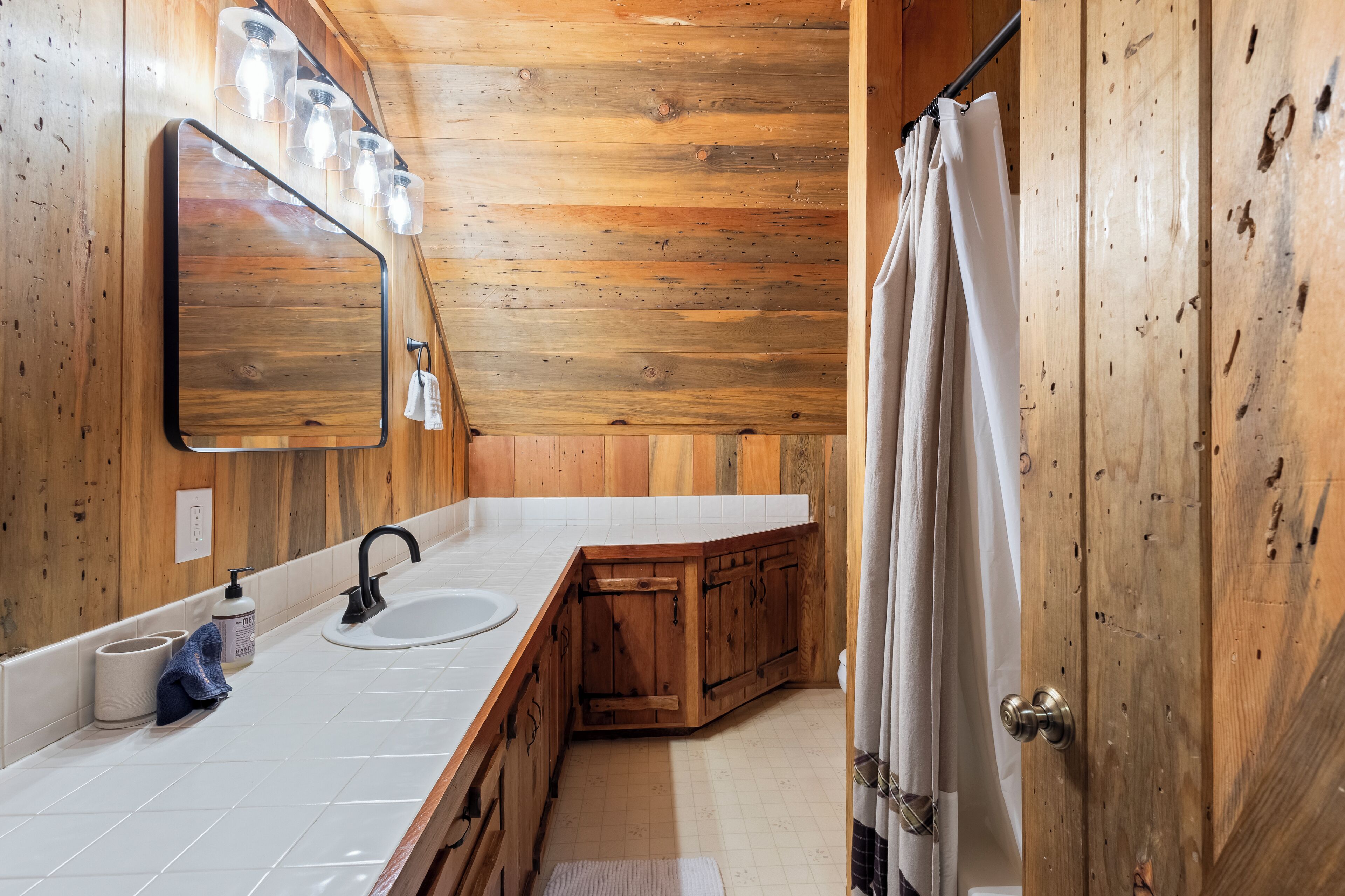 A wooden cabin bathroom with a white sink, a mirror, and a shower curtain.