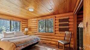Een slaapkamer in een blokhut met een bed, een stoel, een raam en een deur.