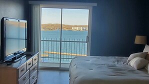 Ein Schlafzimmer mit einem Bett, einem Fernseher auf einer Kommode, einem Deckenventilator und Blick auf ein Gewässer vom Balkon aus.