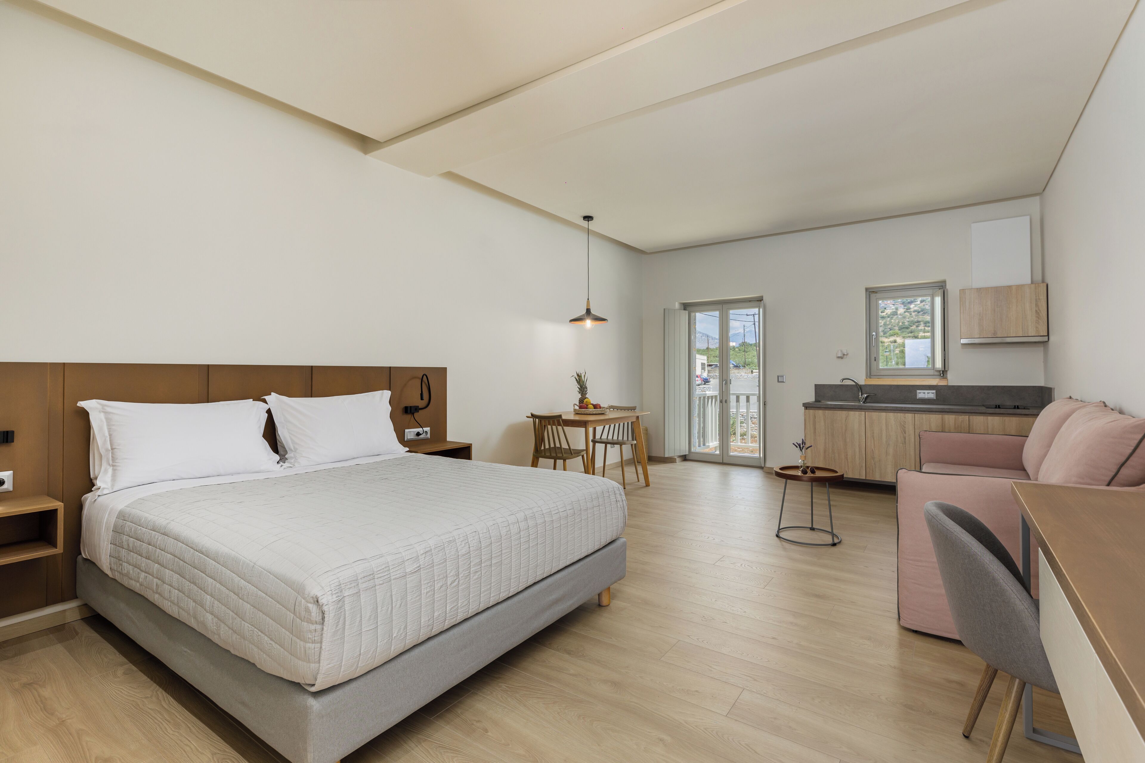 A modern bedroom with a large bed, a desk, and a kitchenette.
