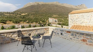 Una terraza con muros de piedra, mobiliario exterior y vistas a un paisaje montañoso.