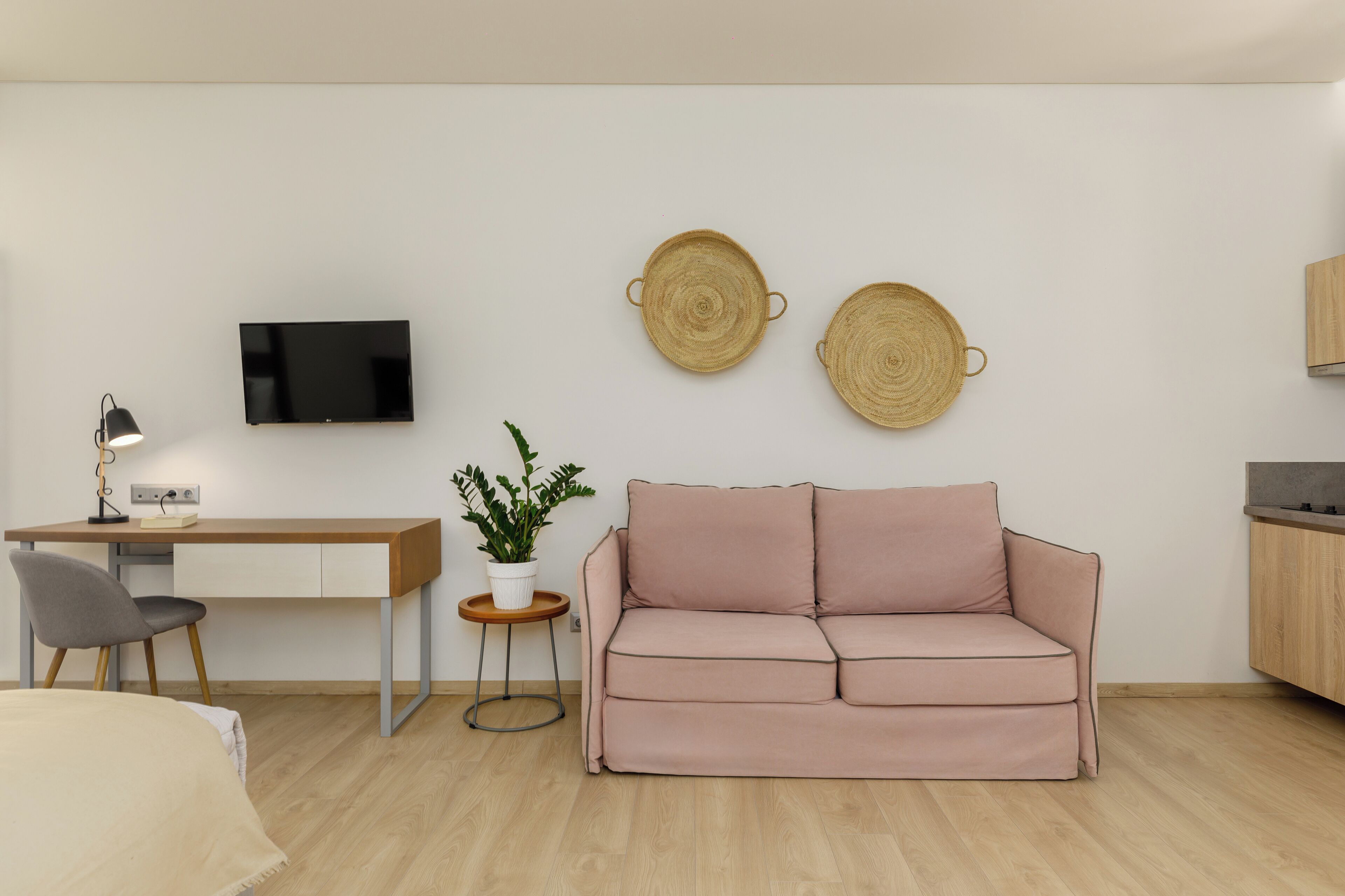 A modern living room with a wooden desk, a pink sofa, a small potted plant, and two woven wall decorations.