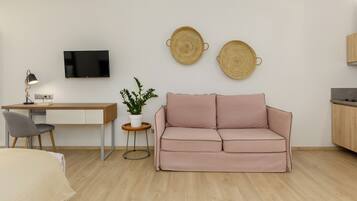A modern living room with a wooden desk, a pink sofa, a small potted plant, and two woven wall decorations.