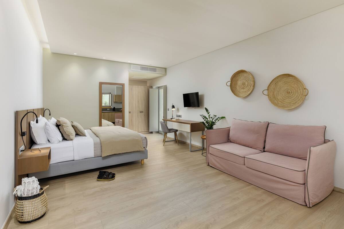 Ein modernes Schlafzimmer mit einem Bett, einem Schreibtisch, einem rosa Sofa und einem Fernseher.
