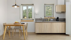 Una cocina moderna con armarios de madera, una mesa de comedor con sillas, una lámpara colgante y vistas a zonas verdes a través de las ventanas.