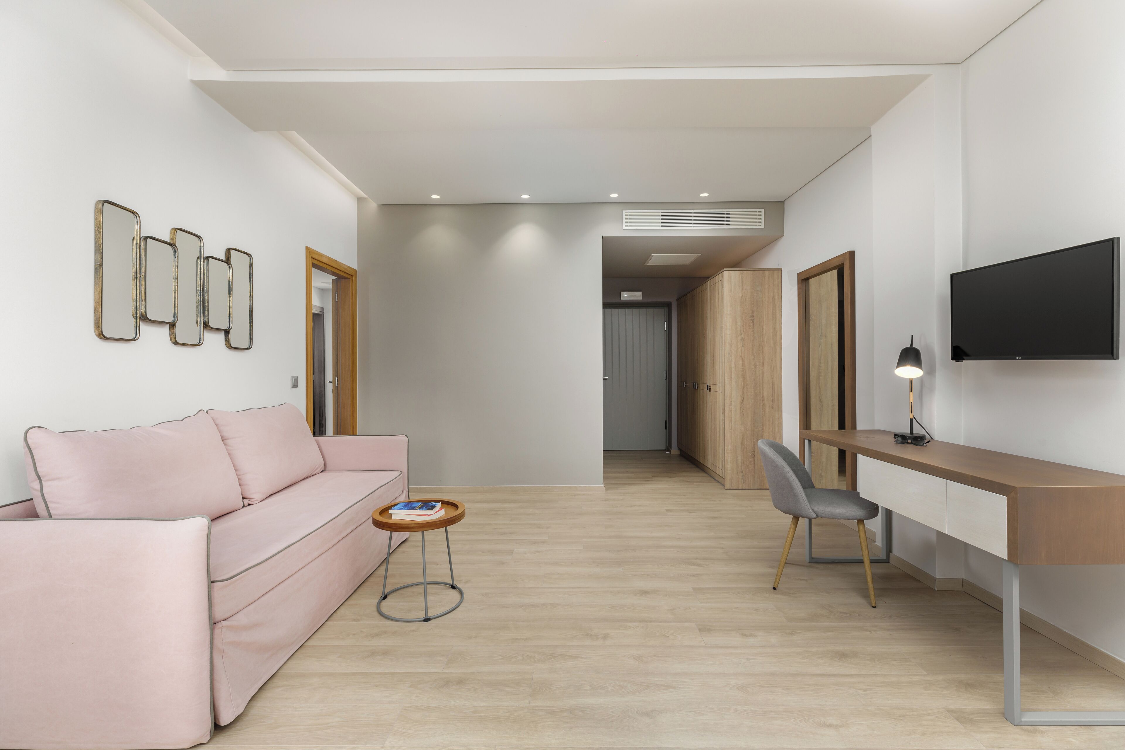 A modern living room with a pink sofa, a wooden desk, and a TV mounted on the wall.