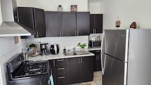 A modern kitchen with dark cabinets, a stainless steel refrigerator, a microwave, a coffee maker, and a gas stove. - Cozy Island Home (Quebradillas)