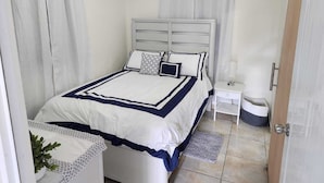 A neatly arranged bedroom with a bed, bedside table, and a small plant. - Cozy Island Home (Quebradillas)