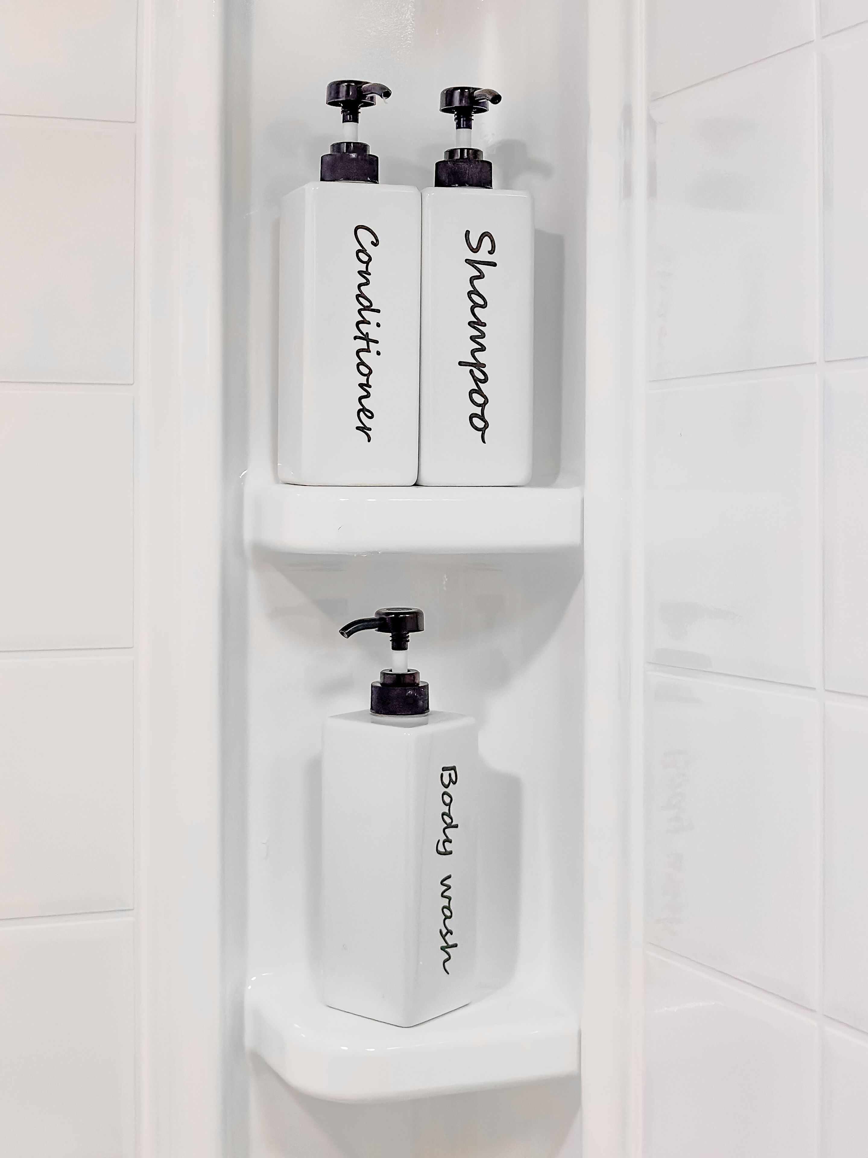 Casa de banho com três prateleiras brancas, cada uma com um frasco de champô, condicionador e gel de banho.