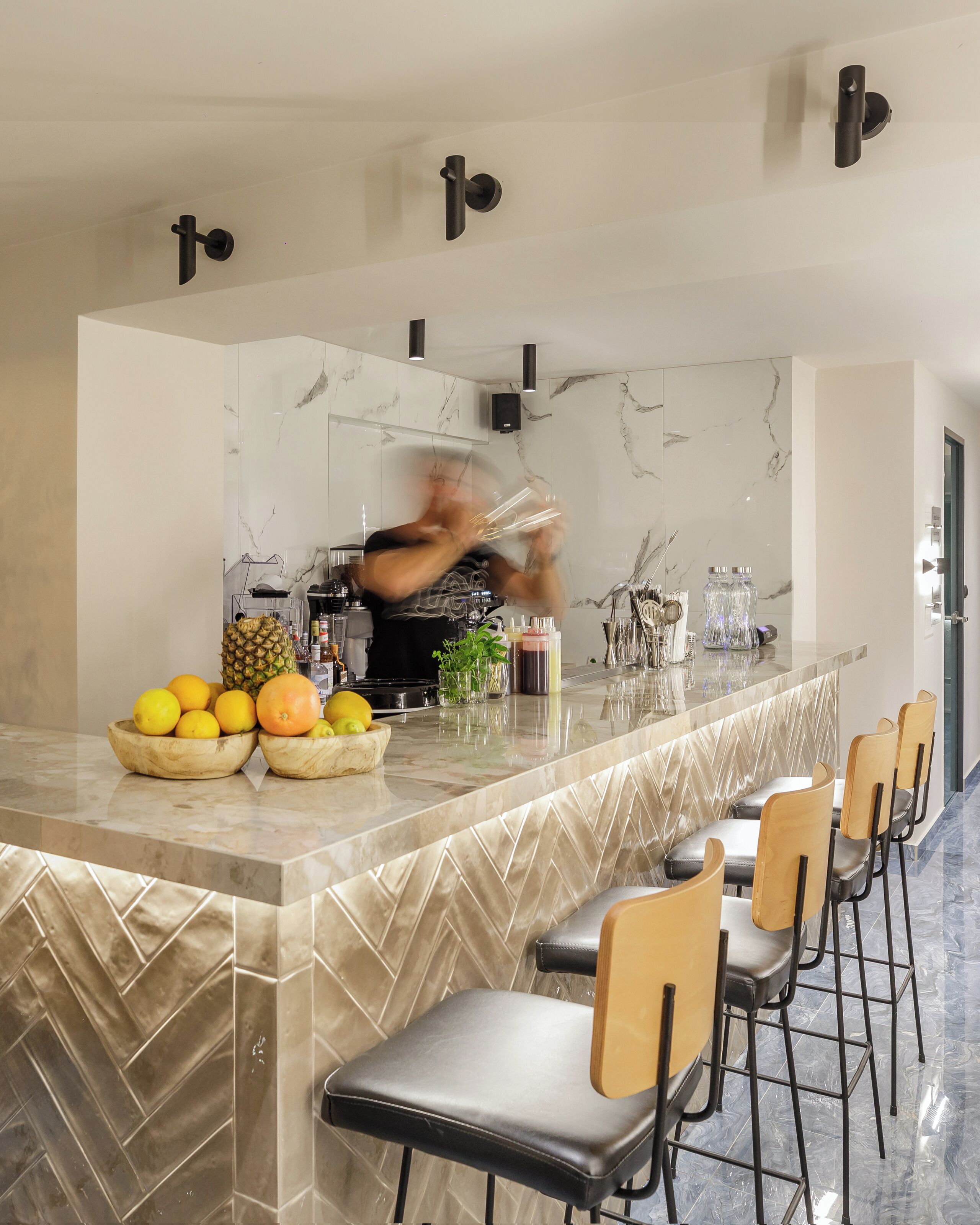 Eine moderne Küche mit Marmor-Spritzschutz, einer zentralen Kochinsel mit Obstschalen und einer Barähnlichen Sitzgelegenheit.