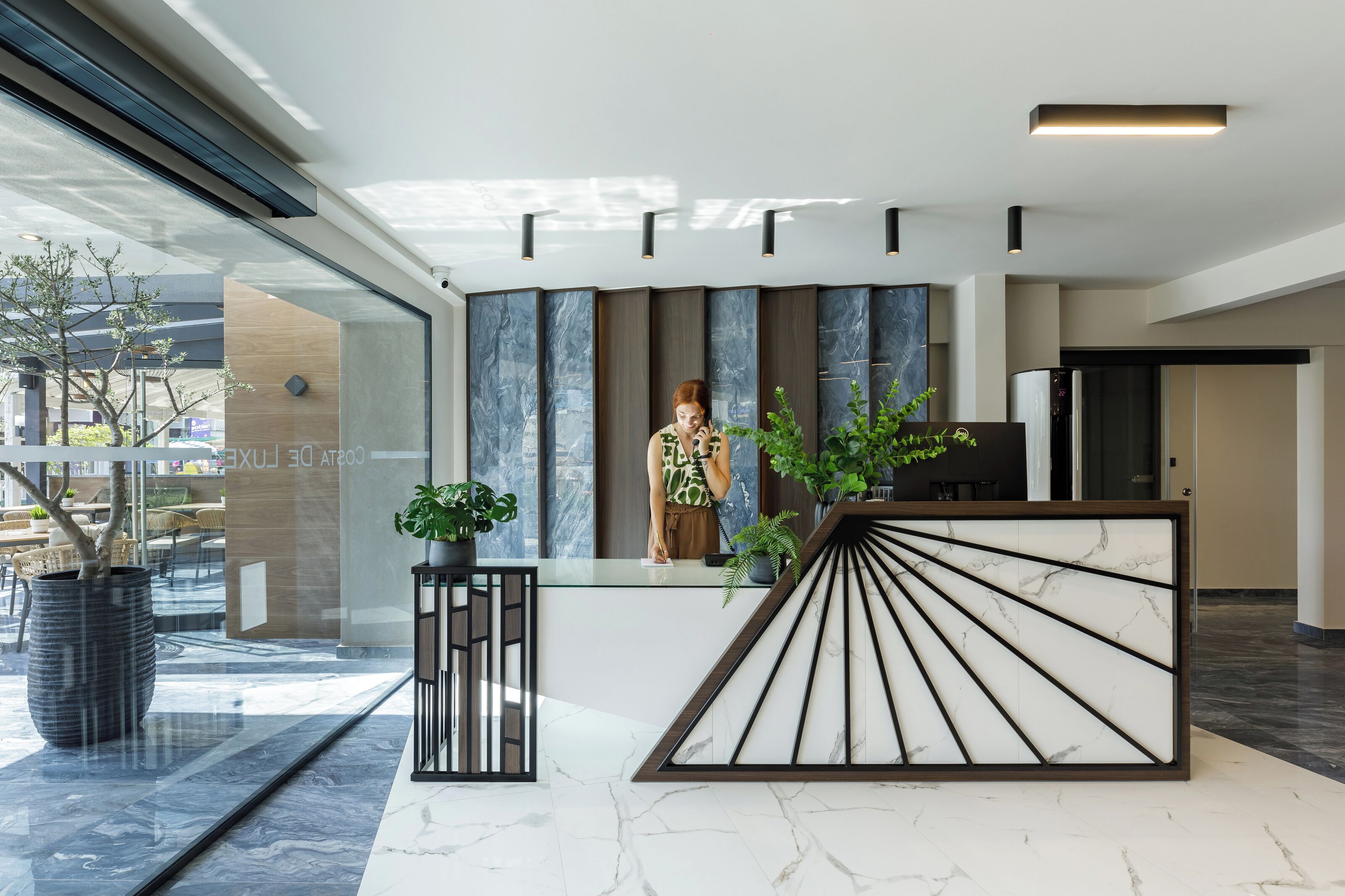 Un área de recepción moderna con suelo de mármol, mostrador de recepción de diseño geométrico y plantas en macetas.