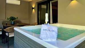 A room with a hot tub, a table with chairs, a potted plant, and a bottle of champagne. - Costa De Luxe Suites (Dio-Olympos)