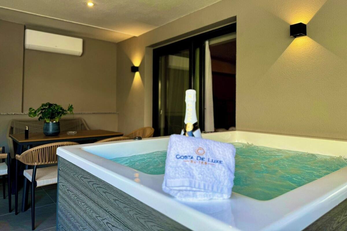 A room with a hot tub, a table with chairs, a potted plant, and a bottle of champagne.