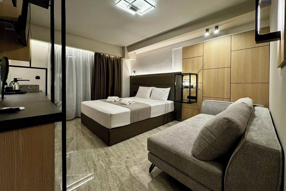 A modern hotel room with a bed, a sofa, a desk, and a mirror.