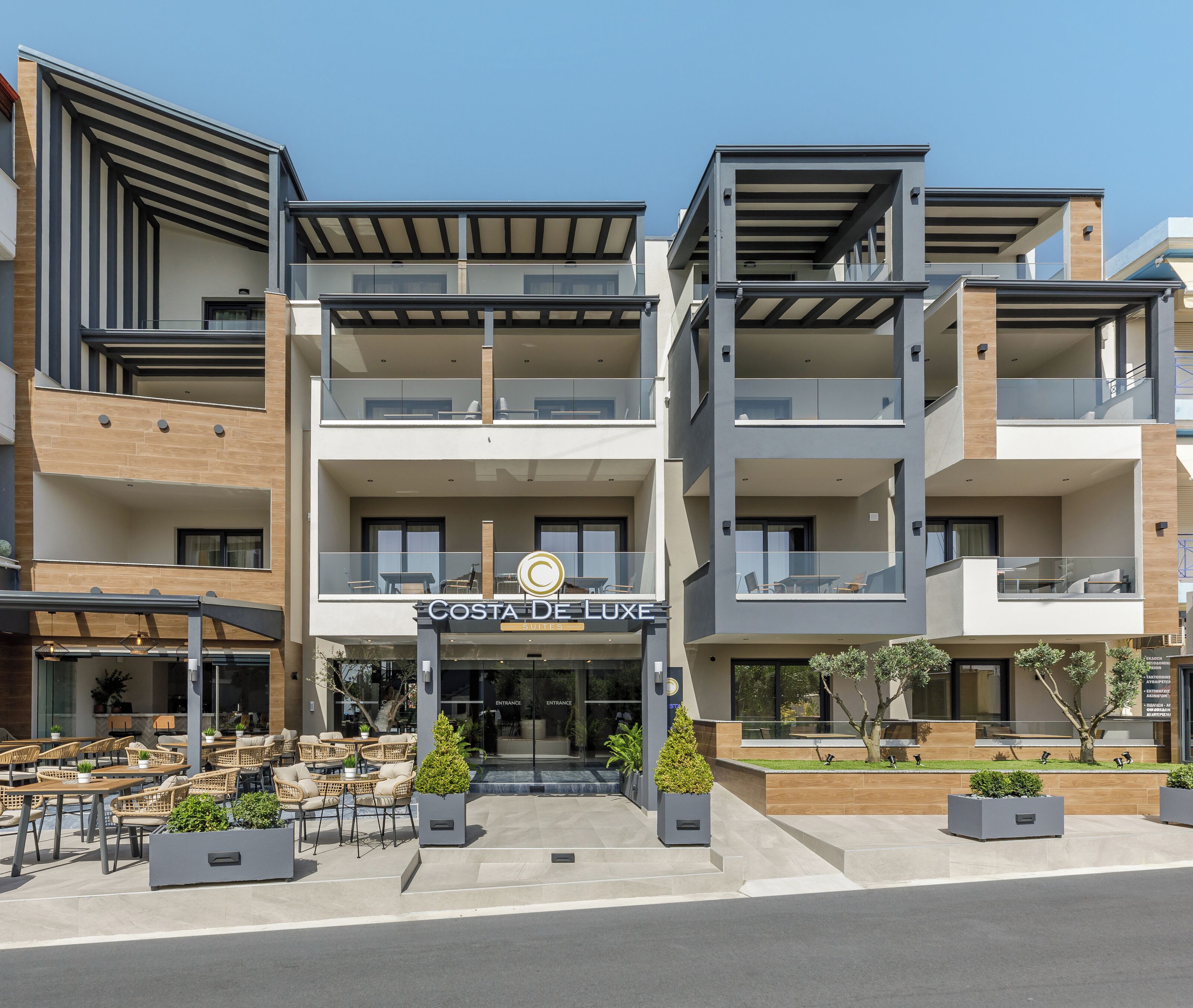 A modern multi-story building with a sign reading "Costa De Luxe Suites".