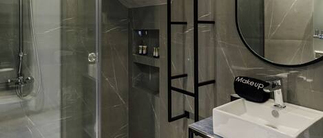 A modern bathroom with a glass-enclosed shower, a white sink, and a mirror above it. There are towels with "Costa de Luxe" branding on the counter.