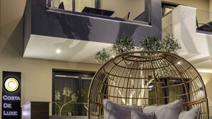A modern hotel lobby with a hanging chair, a lit candle, and a sign for 'Costa de Luxe Suites'. - Costa De Luxe Suites (Dio-Olympos)