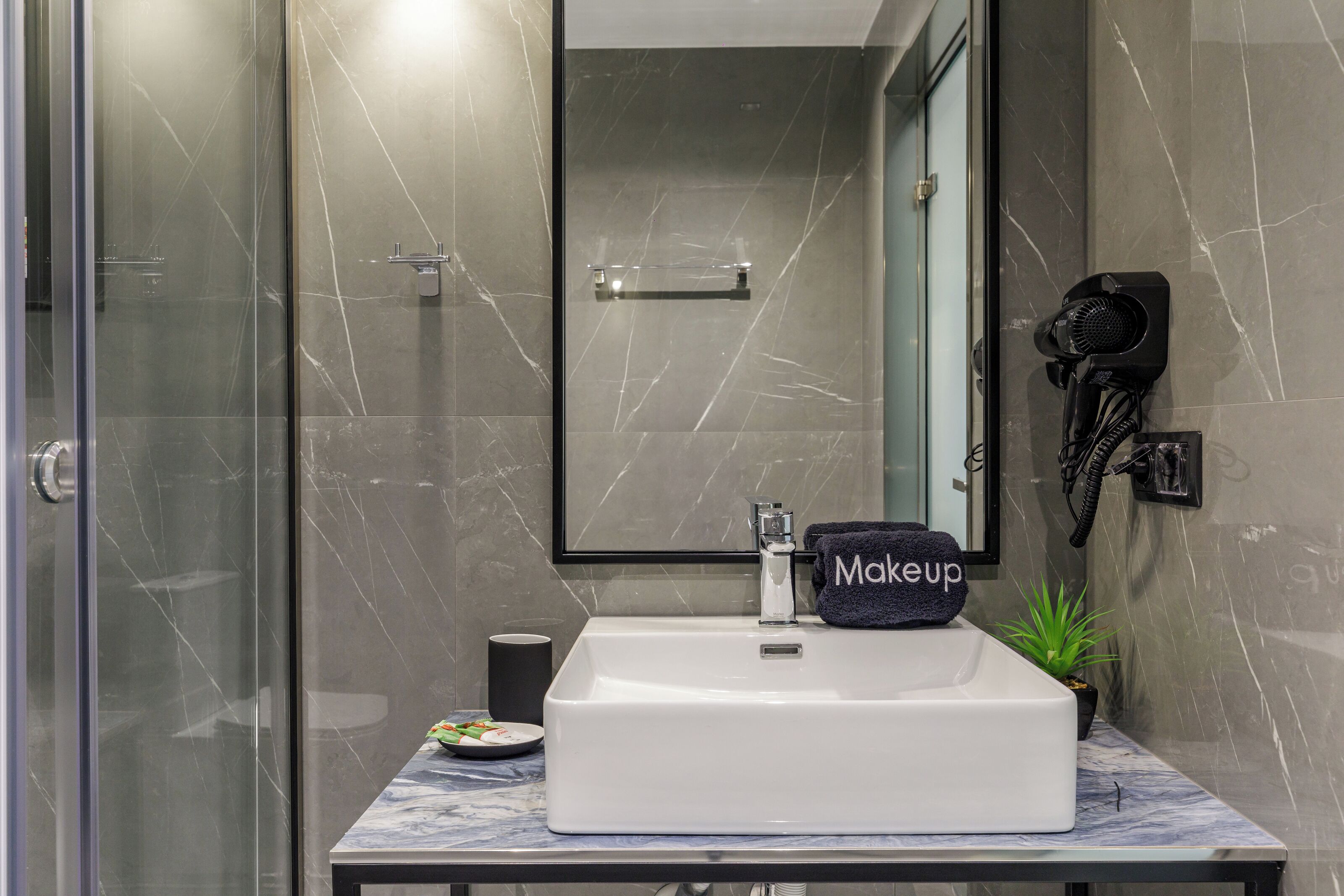 A bathroom with a white sink, a mirror, a hairdryer, and a small potted plant.
