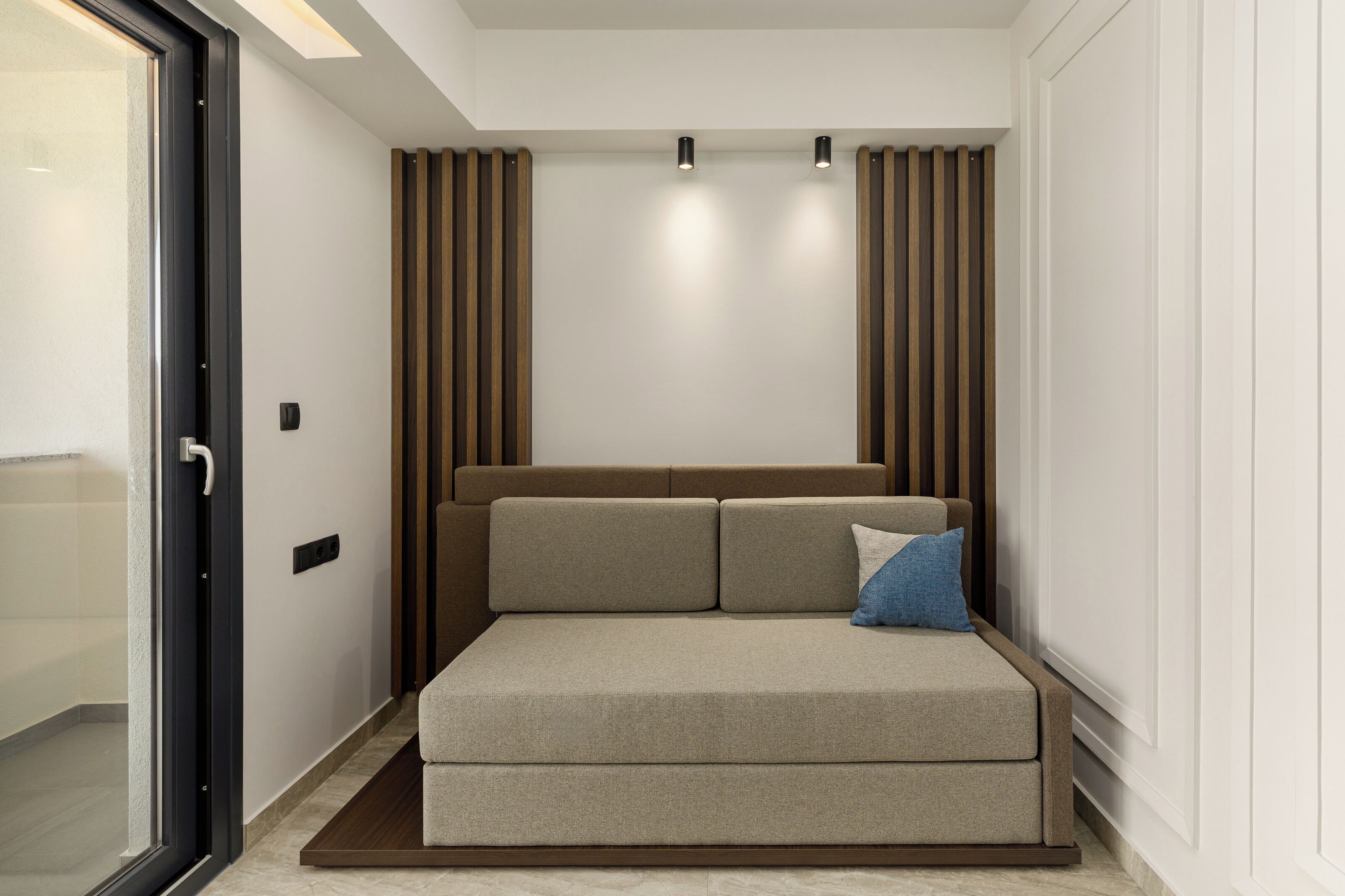 A modern bedroom with a sofa bed, a glass door, and wooden paneling on the walls.