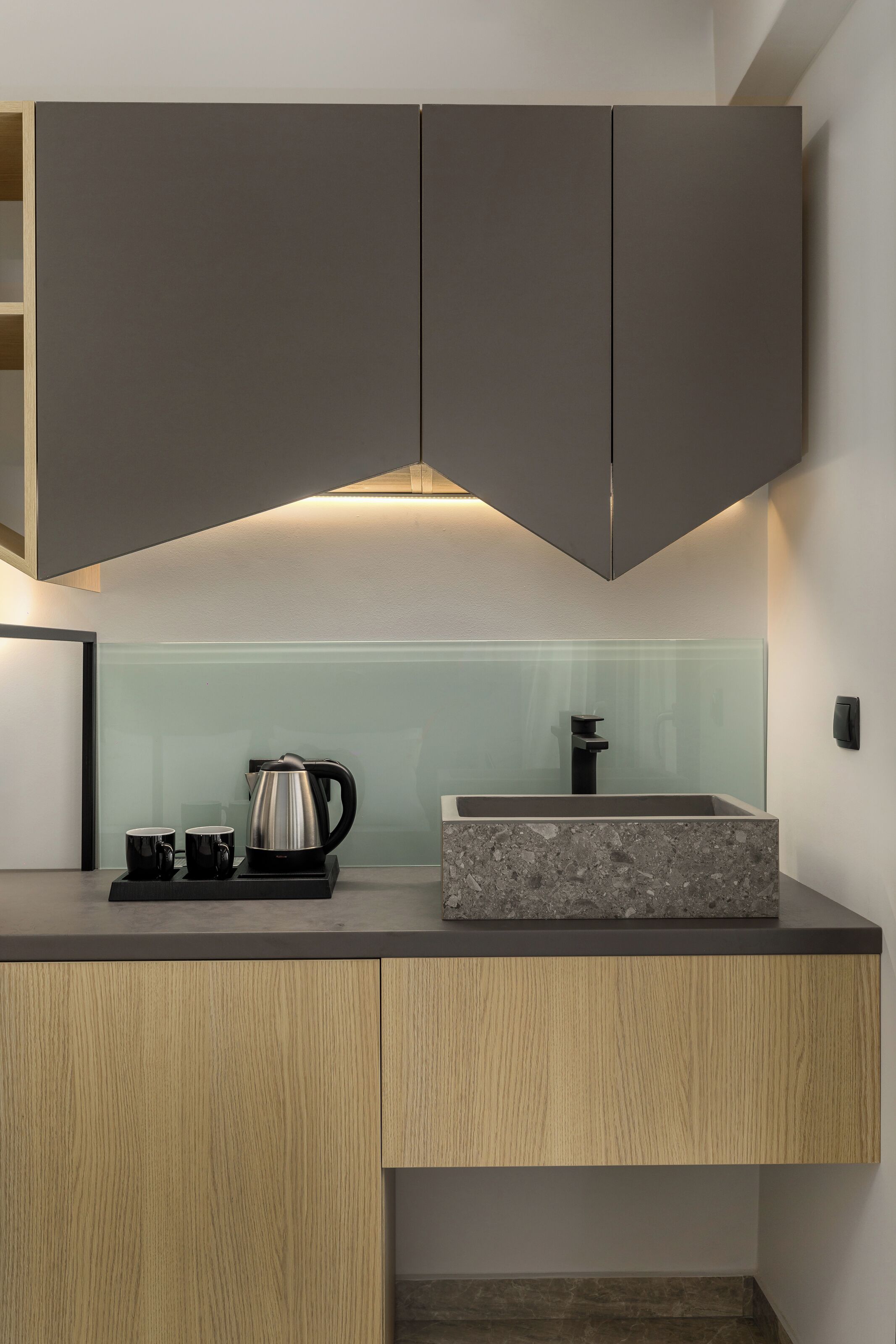 A modern kitchen with dark cabinets, a marble countertop, a coffee maker, and a sink.